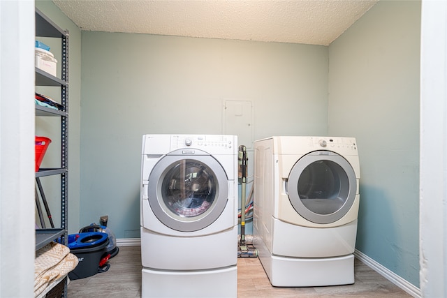 clothes washing area with light wood-type flooring, a textured ceiling, and washer and dryer