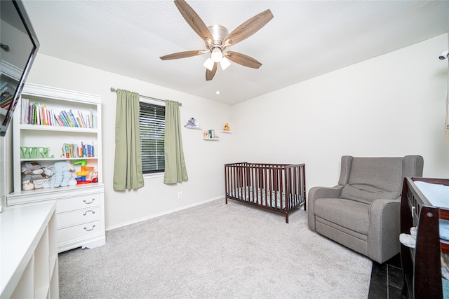 carpeted bedroom featuring ceiling fan, a textured ceiling, and a nursery area