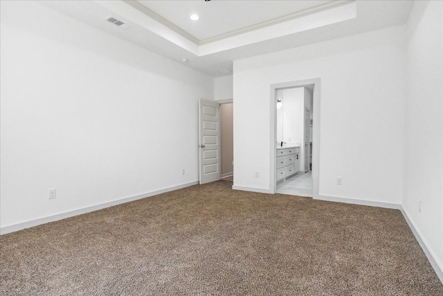 unfurnished bedroom with ensuite bathroom, light colored carpet, and a raised ceiling