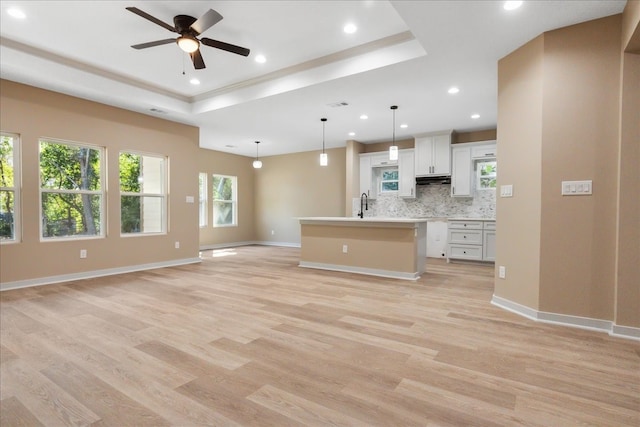 kitchen with light hardwood / wood-style floors, a center island with sink, white cabinets, pendant lighting, and decorative backsplash