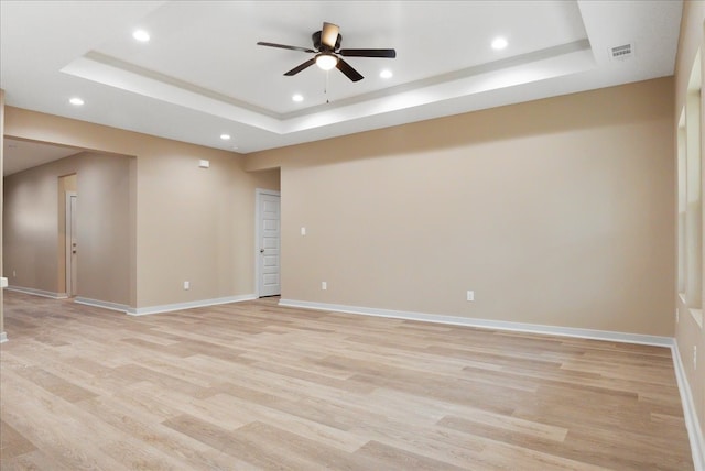 empty room with light hardwood / wood-style flooring, ceiling fan, and a raised ceiling