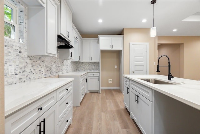 kitchen featuring light stone counters, white cabinets, sink, light hardwood / wood-style flooring, and decorative light fixtures