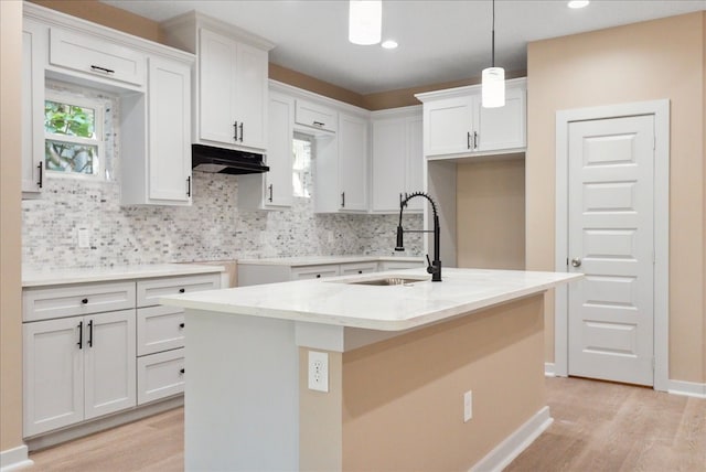 kitchen featuring decorative light fixtures, white cabinetry, sink, and a center island with sink