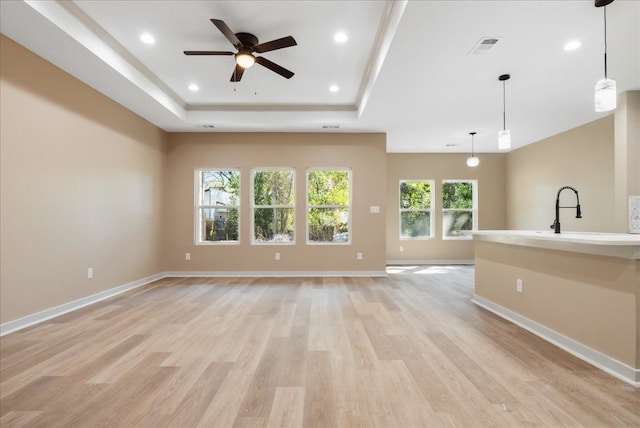 unfurnished living room with sink, a raised ceiling, ceiling fan, and light hardwood / wood-style flooring