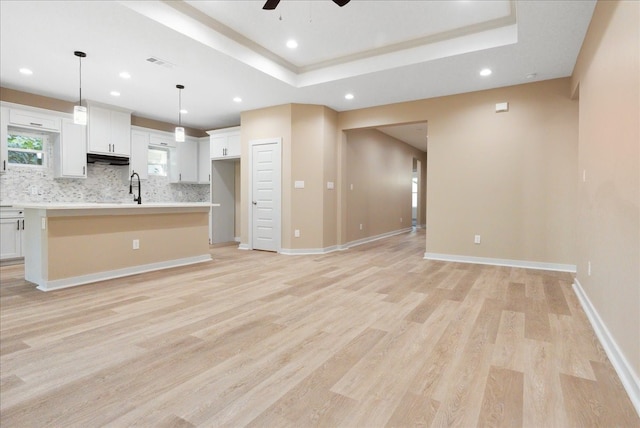 kitchen with tasteful backsplash, pendant lighting, light hardwood / wood-style floors, white cabinets, and a kitchen island with sink