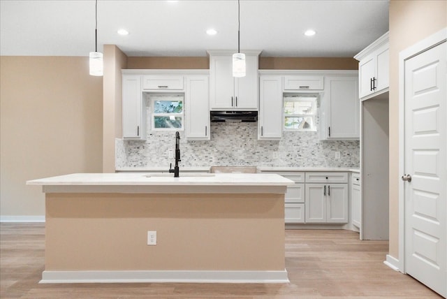 kitchen with sink, hanging light fixtures, a kitchen island with sink, white cabinets, and light wood-type flooring