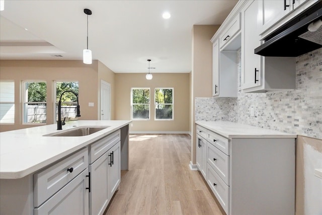 kitchen featuring tasteful backsplash, white cabinetry, hanging light fixtures, sink, and light hardwood / wood-style floors