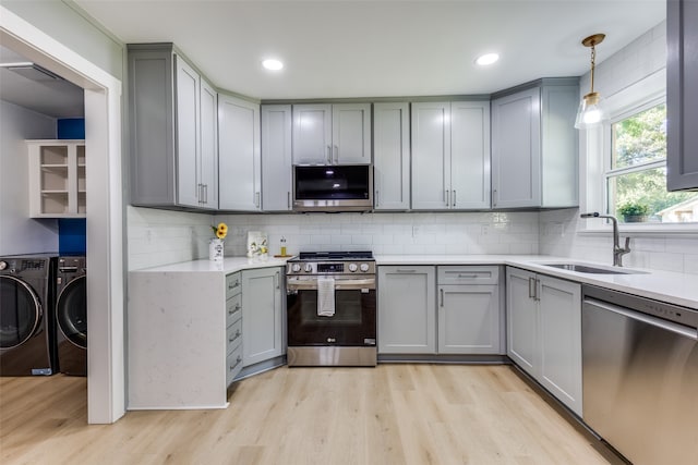 kitchen featuring light hardwood / wood-style floors, appliances with stainless steel finishes, decorative light fixtures, washer and clothes dryer, and gray cabinetry