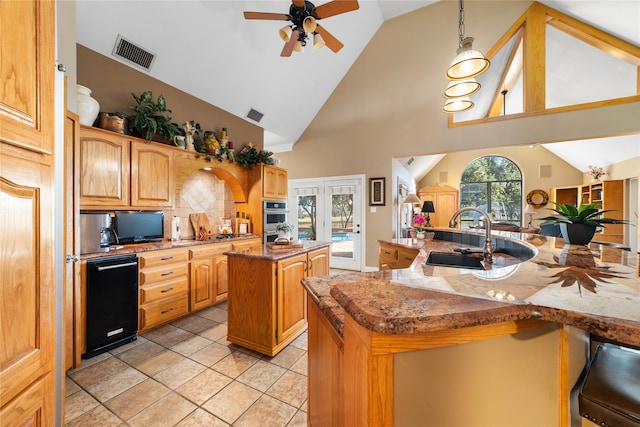 kitchen with high vaulted ceiling, decorative light fixtures, a center island with sink, and light stone counters