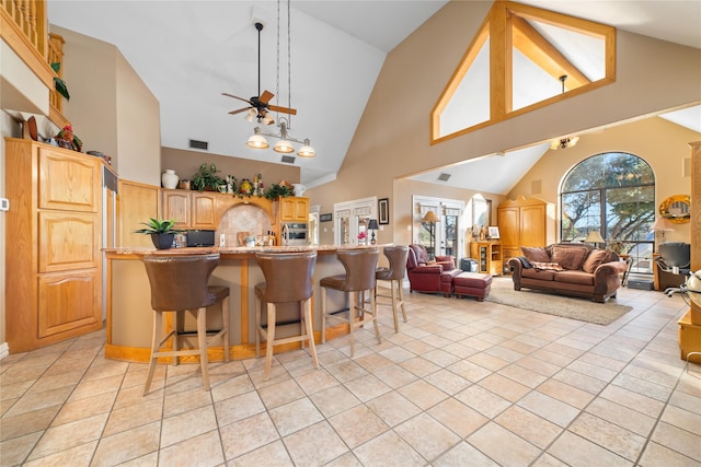 kitchen featuring ceiling fan, a kitchen bar, light tile patterned floors, and high vaulted ceiling