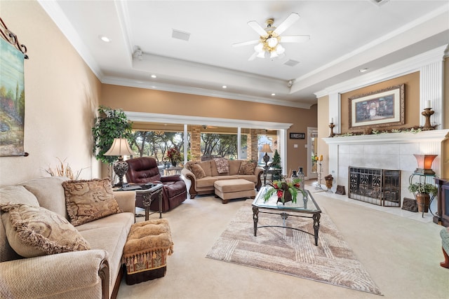 carpeted living room with ornamental molding, a tray ceiling, ceiling fan, and a fireplace