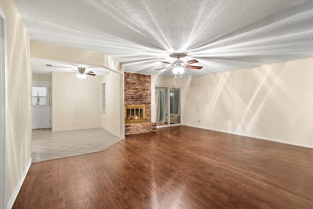 unfurnished living room featuring a fireplace, wood-type flooring, ceiling fan, and a textured ceiling