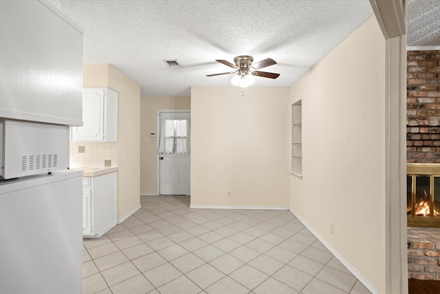 interior space with a brick fireplace, ceiling fan, a textured ceiling, and light tile patterned floors