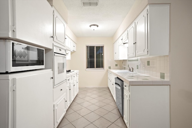 kitchen with tile counters, stainless steel appliances, white cabinets, and sink