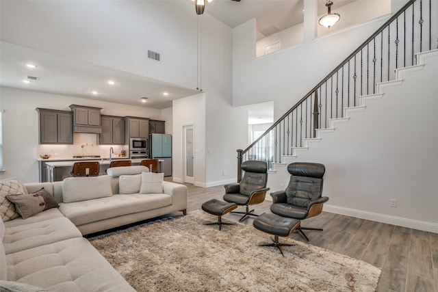 living room featuring a towering ceiling, ceiling fan, and light wood-type flooring