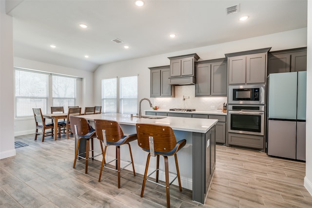 kitchen featuring a kitchen bar, light hardwood / wood-style floors, a center island with sink, sink, and appliances with stainless steel finishes