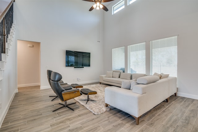 living room with a towering ceiling, light hardwood / wood-style floors, and ceiling fan