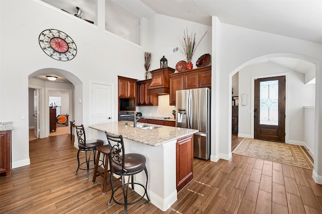 kitchen with appliances with stainless steel finishes, dark wood-type flooring, an island with sink, and light stone countertops