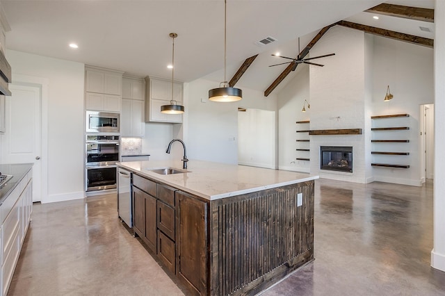 kitchen featuring a large fireplace, sink, an island with sink, pendant lighting, and appliances with stainless steel finishes