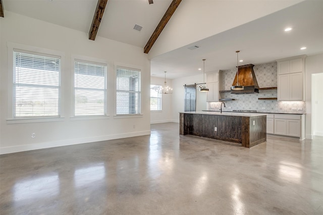 kitchen with vaulted ceiling with beams, decorative backsplash, decorative light fixtures, a kitchen island with sink, and custom exhaust hood