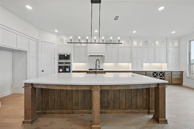 4029 Trellis Dr, Celina, TX 75078 - kitchen with appliances with stainless steel finishes, tasteful backsplash, a spacious island, light wood-type flooring, and custom exhaust hood