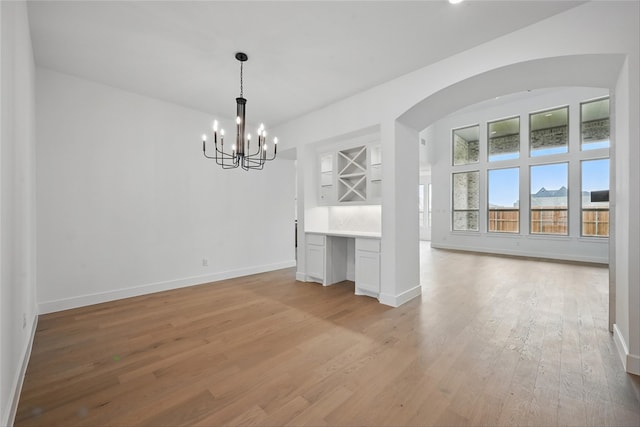 4029 Trellis Dr, Celina, TX 75078 - unfurnished dining area featuring a chandelier, light wood-style floors, arched walkways, and baseboards