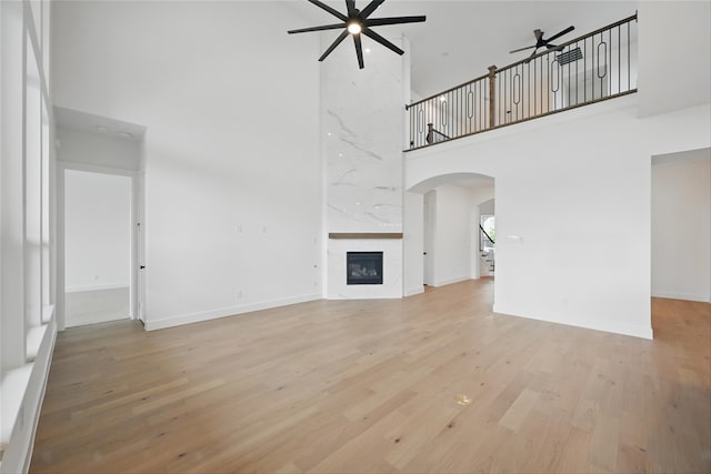 4029 Trellis Dr, Celina, TX 75078 - unfurnished living room with ceiling fan, a towering ceiling, arched walkways, wood finished floors, and a high end fireplace