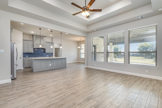 kitchen with decorative light fixtures, gray cabinets, a tray ceiling, and an island with sink