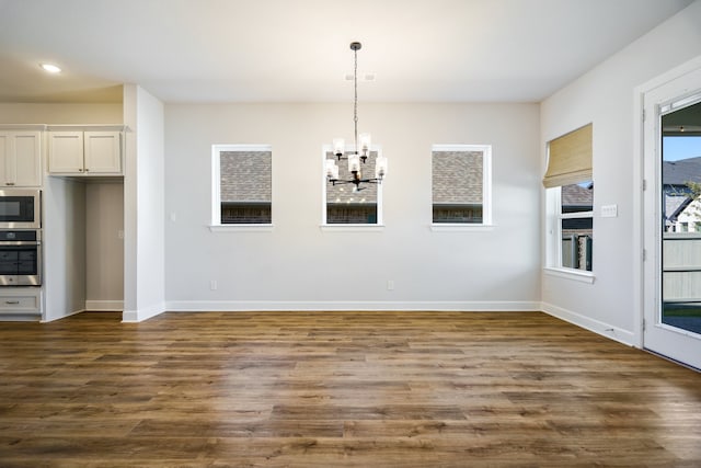 unfurnished dining area featuring dark wood-type flooring and an inviting chandelier