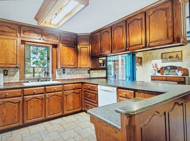 kitchen featuring dark stone counters, white dishwasher, kitchen peninsula, sink, and tasteful backsplash