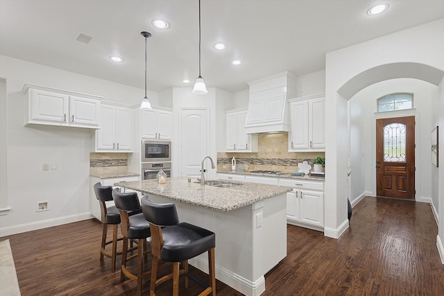 kitchen featuring white cabinetry, sink, light stone counters, appliances with stainless steel finishes, and an island with sink