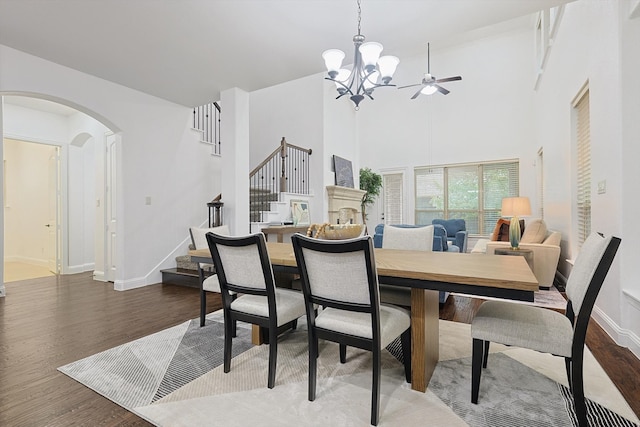 dining room featuring ceiling fan with notable chandelier, hardwood / wood-style flooring, and a towering ceiling