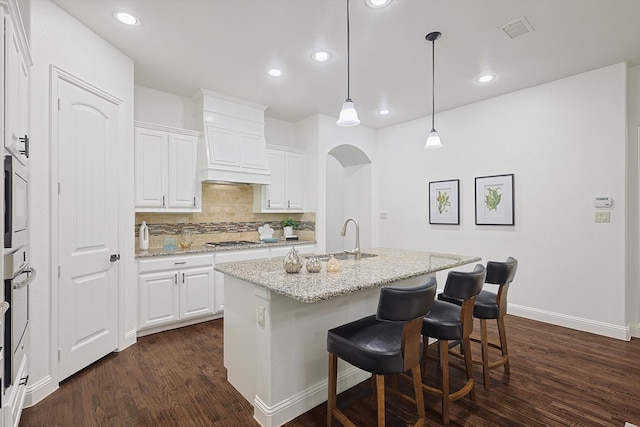 kitchen featuring white cabinetry, decorative light fixtures, light stone counters, and a center island with sink