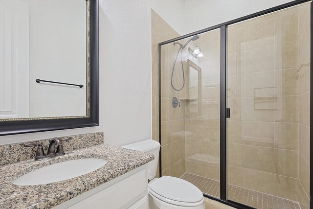 bathroom featuring a shower with shower door, vanity, and toilet