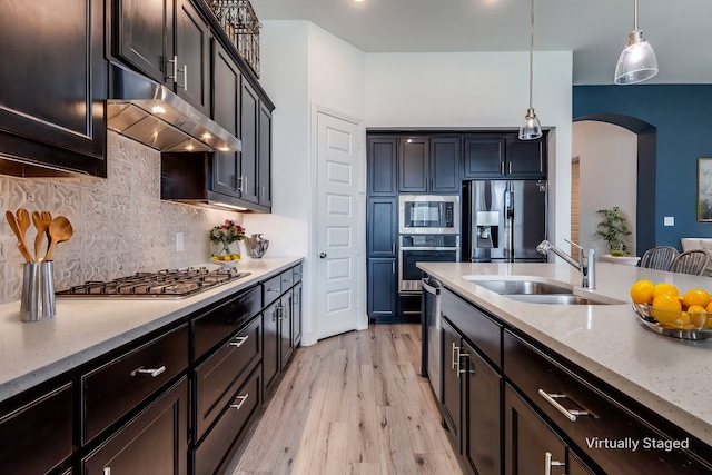 kitchen with light stone counters, appliances with stainless steel finishes, decorative light fixtures, sink, and light hardwood / wood-style floors