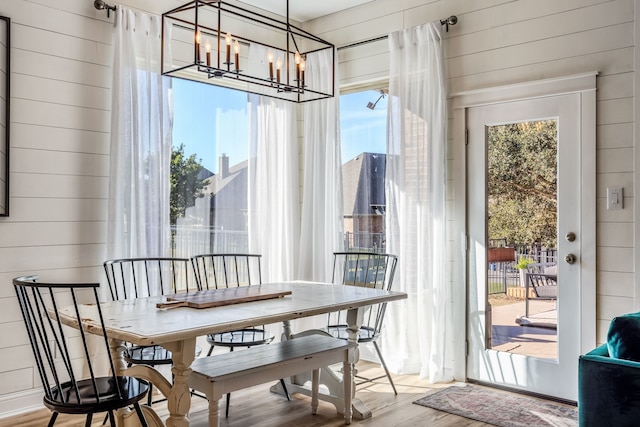 dining space featuring light hardwood / wood-style floors, wood walls, and a notable chandelier