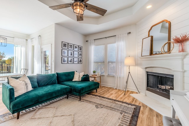 living room featuring wood-type flooring, ceiling fan, and a raised ceiling