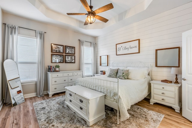 bedroom featuring ceiling fan, multiple windows, light wood-type flooring, and a tray ceiling