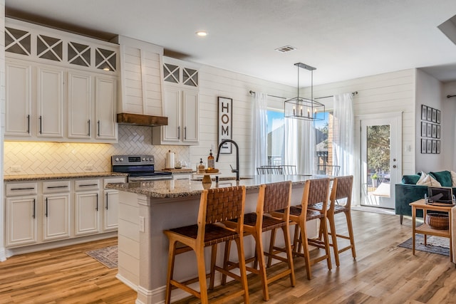 kitchen with white cabinets, stainless steel range with electric cooktop, decorative light fixtures, and a kitchen island with sink