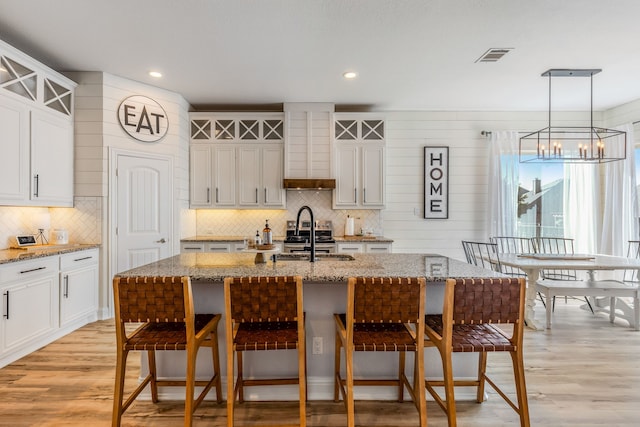 kitchen with white cabinetry, a center island with sink, and a chandelier