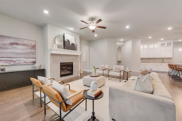 living room featuring a tiled fireplace, light hardwood / wood-style flooring, and ceiling fan