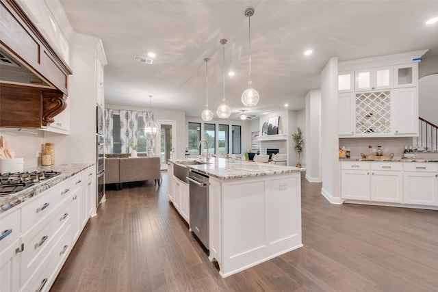 kitchen with stainless steel appliances, white cabinets, decorative light fixtures, and a kitchen island with sink