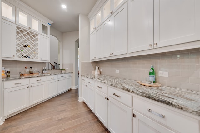 kitchen featuring tasteful backsplash, light stone counters, light hardwood / wood-style floors, and white cabinets