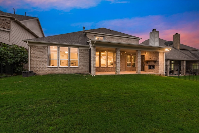 back house at dusk with a lawn and a patio area