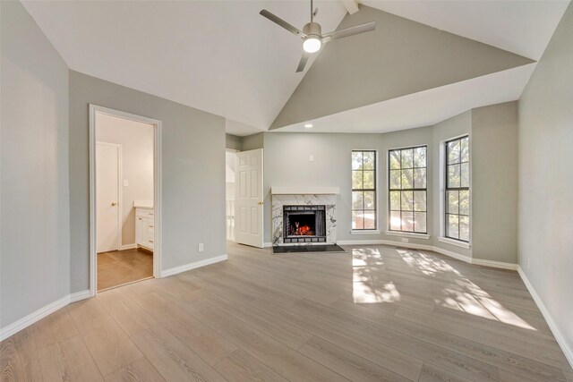 unfurnished living room featuring ceiling fan, light wood-type flooring, high vaulted ceiling, and a premium fireplace