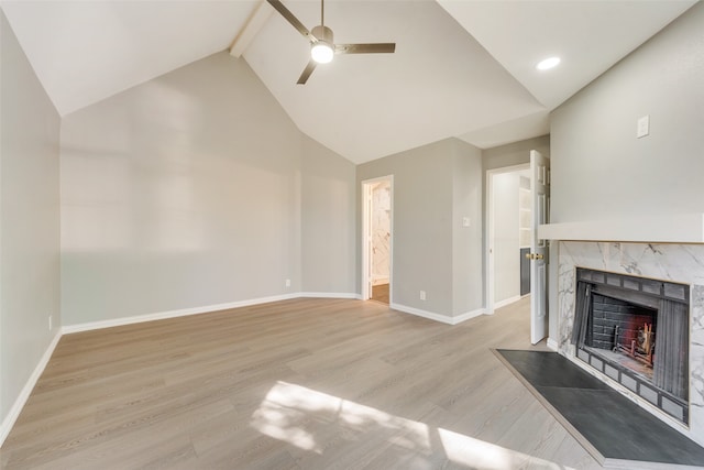 unfurnished living room with a high end fireplace, ceiling fan, beam ceiling, high vaulted ceiling, and light hardwood / wood-style flooring