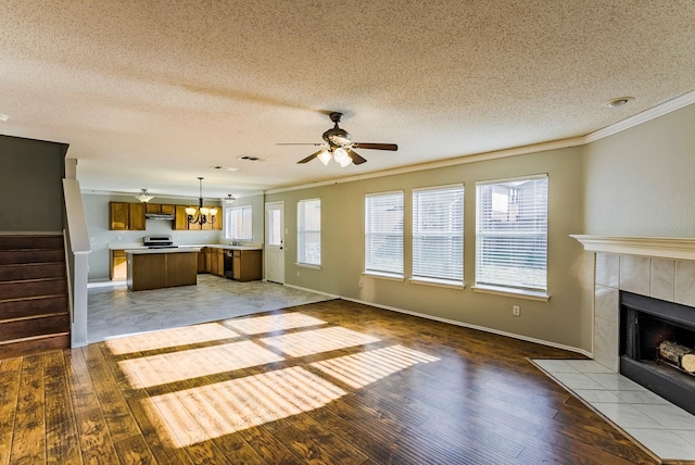 unfurnished living room featuring ceiling fan with notable chandelier, a tiled fireplace, a textured ceiling, ornamental molding, and light hardwood / wood-style flooring