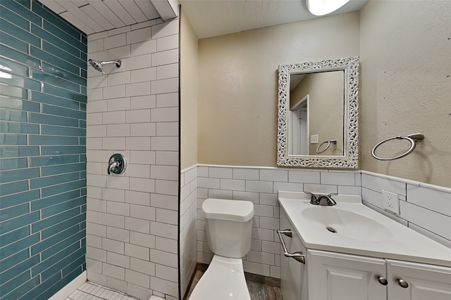 bathroom with toilet, vanity, tile walls, and tiled shower