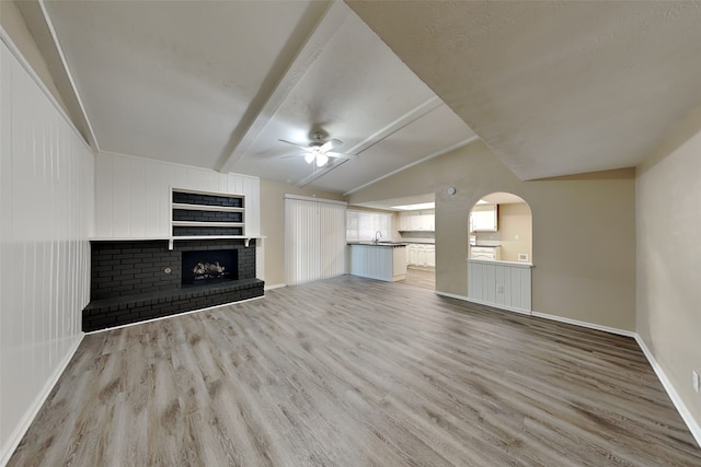 unfurnished living room with ceiling fan, sink, light hardwood / wood-style flooring, and vaulted ceiling with beams