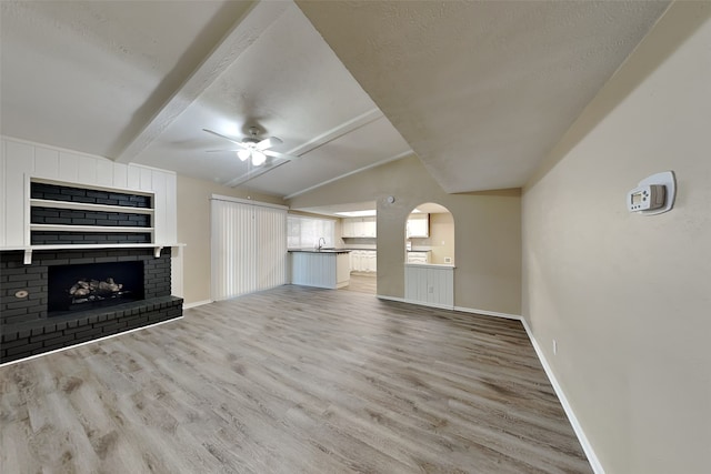 unfurnished living room with a brick fireplace, light wood-type flooring, vaulted ceiling with beams, and sink